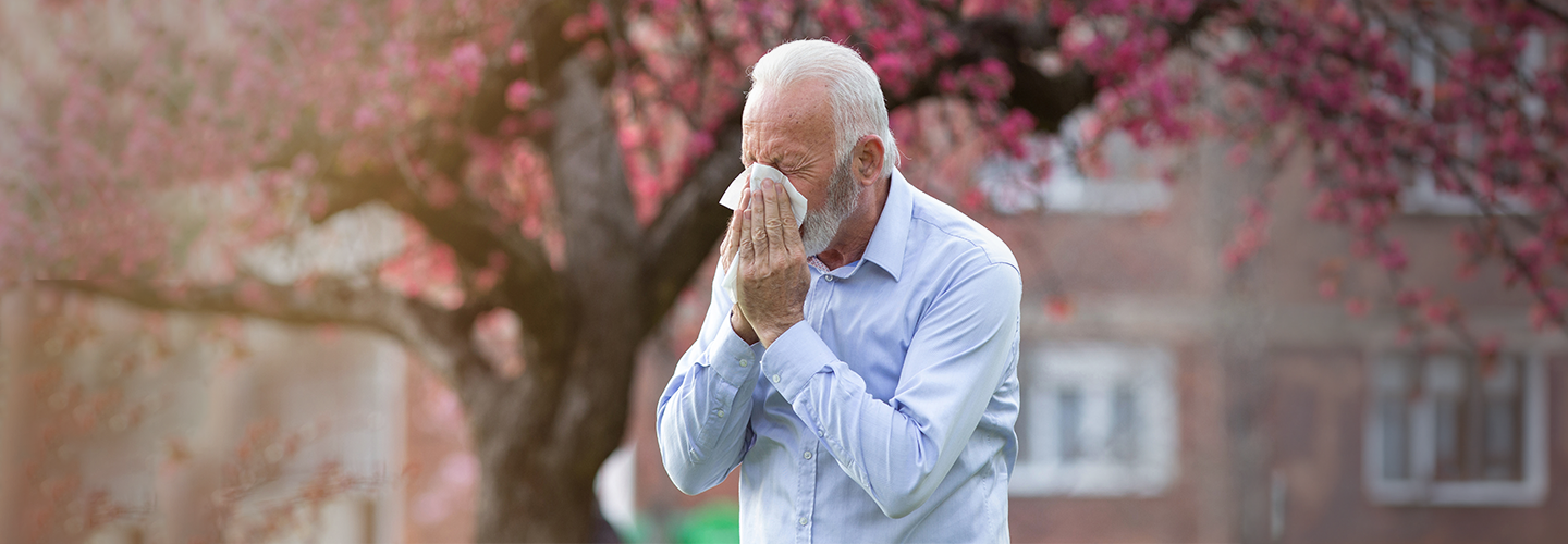 Personne se mouchant à l’extérieur devant des arbres en fleurs