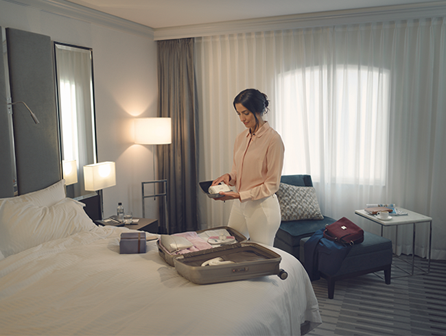  Personne préparant une valise dans une chambre et rangeant un appareil PPC de voyage AirMini avant un déplacement.