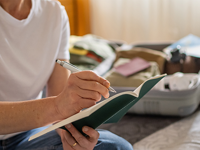 Un voyageur préparant une liste pour vérifier ce qu’il emporte à côté d’une valise ouverte, en s’assurant d’avoir préparé son appareil PPC ainsi que les articles essentiels pour un voyage sans stress