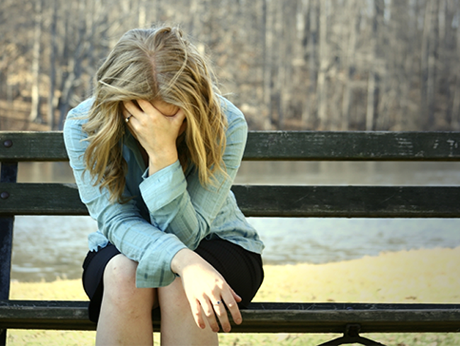  femme assise seule sur un banc dans un parc, la tête appuyée sur une main, illustrant une sensation de fatigue diurne.