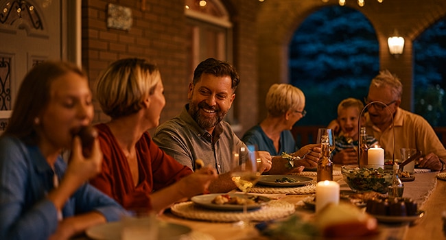 Plusieurs personnes partagent un repas en plein air autour d’une grande table éclairée à la bougie lors d’une soirée d’été.