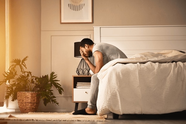  Un homme assis au bord de son lit, épuisé par une mauvaise nuit de sommeil.